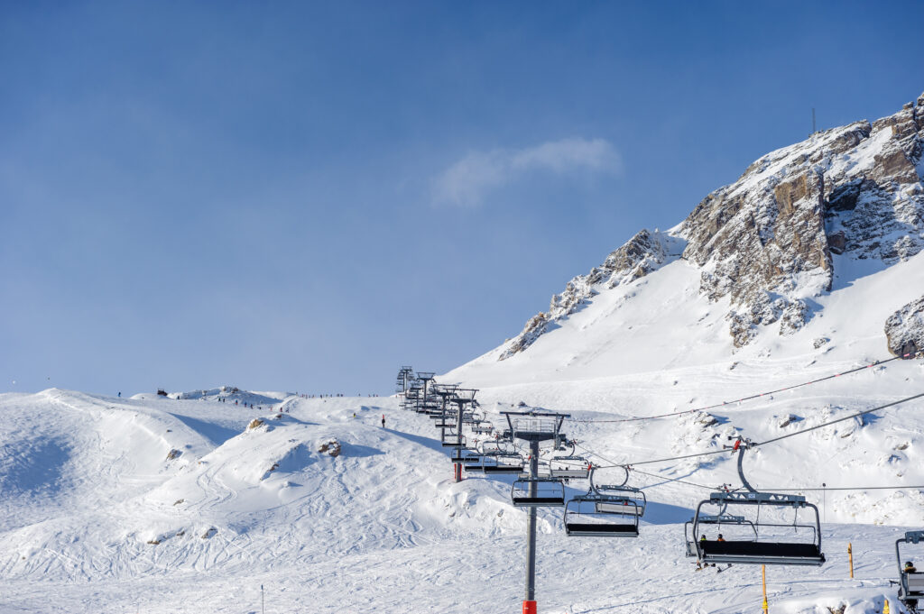 Ski lift in mountains at winter. Alpine winter mountain landscape. French Alps covered with snow in sunny day. Val-d'Isere, Alps, France